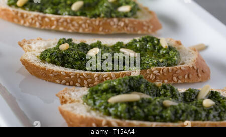 Bruschetta con pesto di basilico sauace e pinoli, su una piastra bianca. Cibo sano, la dieta e il concetto di cucina a vista. Specialità della cucina italiana. Sof selettiva Foto Stock