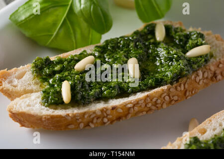 Bruschetta con pesto di basilico sauace e pinoli, su una piastra bianca. Cibo sano, la dieta e il concetto di cucina a vista. Specialità della cucina italiana. Sof selettiva Foto Stock