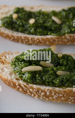 Bruschetta con pesto di basilico sauace e pinoli, su una piastra bianca. Cibo sano, la dieta e il concetto di cucina a vista. Specialità della cucina italiana. Sof selettiva Foto Stock