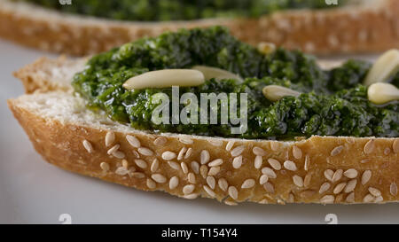 Bruschetta con pesto di basilico sauace e pinoli, su una piastra bianca. Cibo sano, la dieta e il concetto di cucina a vista. Specialità della cucina italiana. Sof selettiva Foto Stock