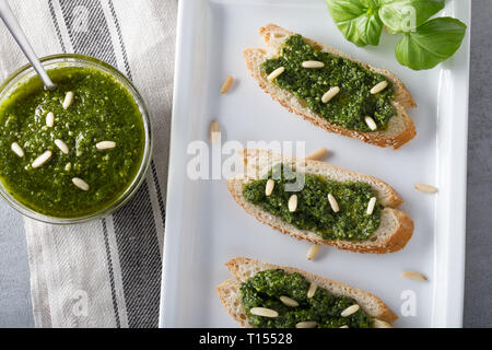 Bruschetta con pesto di basilico sauace e pinoli, su una piastra bianca. Cibo sano, la dieta e il concetto di cucina a vista. Specialità della cucina italiana. Sof selettiva Foto Stock