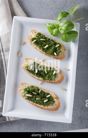 Bruschetta con pesto di basilico sauace e pinoli, su una piastra bianca. Cibo sano, la dieta e il concetto di cucina a vista. Specialità della cucina italiana. Sof selettiva Foto Stock