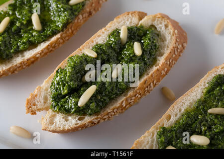 Bruschetta con pesto di basilico sauace e pinoli, su una piastra bianca. Cibo sano, la dieta e il concetto di cucina a vista. Specialità della cucina italiana. Sof selettiva Foto Stock