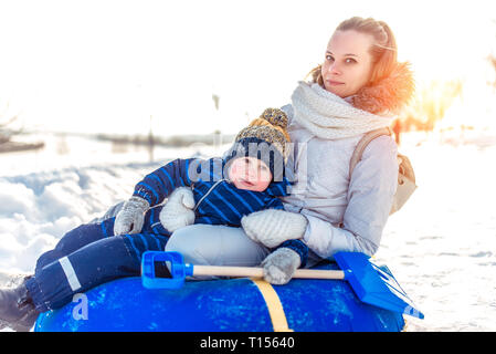 Bello e giovane famiglia, felice mamma e piccolo figlio boy 3-5 anni. In inverno, nel resort in città il resto su tubi gonfiabili giocattolo. Nelle mani della pala Foto Stock