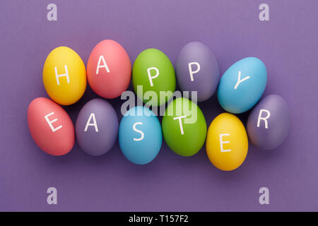 Verniciato colorato uova con lettere disposte in felice Pasqua saluto su sfondo viola. Concetto di vacanza. Foto Stock