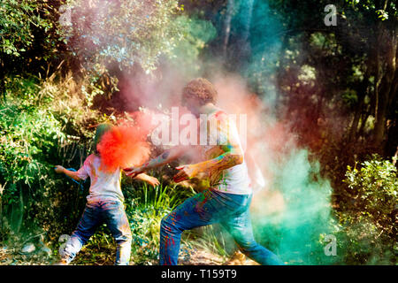 La famiglia felice celebrare Holi festival nella foresta, gettando colorati di vernice in polvere Foto Stock