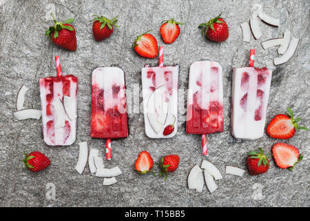 In casa di cocco fragola ghiaccioli con fragole fresche e fette di noce di cocco sul granito Foto Stock