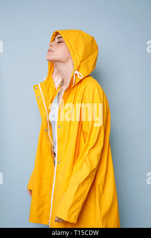 Giovane donna indossa giallo cappotto di pioggia di fronte a sfondo blu Foto Stock