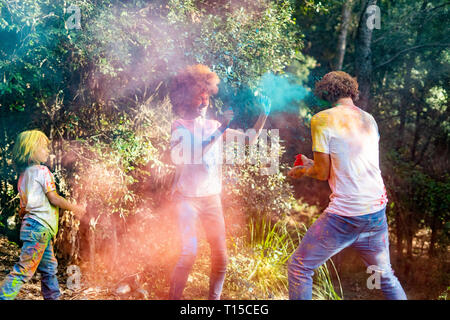 La famiglia felice celebrare Holi festival nella foresta, gettando colorati di vernice in polvere Foto Stock