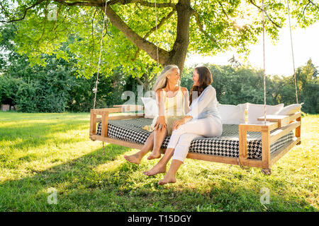 Due donne rilassante su un letto sospeso in giardino Foto Stock