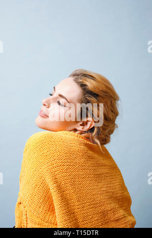 Sorridente giovane donna indossa maglia gialla nella parte anteriore di sfondo blu Foto Stock