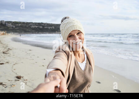 Spagna, Menorca, ritratto di felice donna senior tenendo la mano sulla spiaggia in inverno Foto Stock