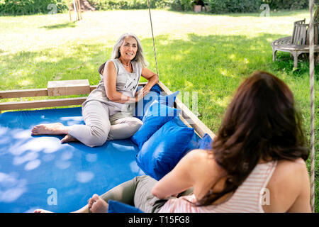 Due donne rilassante su un letto sospeso in giardino Foto Stock