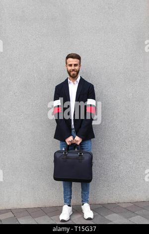 Ritratto di imprenditore elegante in piedi di fronte a muro grigio Foto Stock