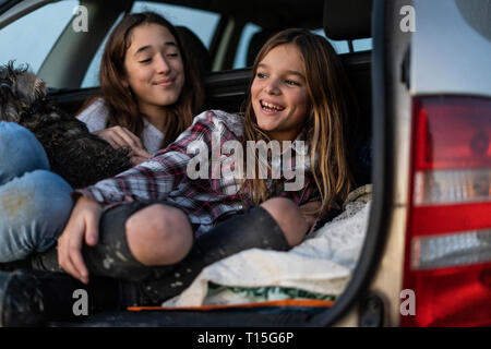 Due sorelle nel bagagliaio della macchina parcheggiata a guardare il tramonto Foto Stock