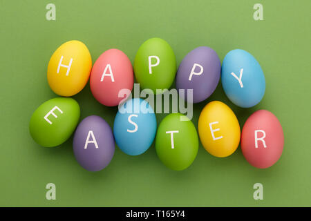 Verniciato colorato uova con lettere disposte in felice Pasqua saluto su sfondo verde. Concetto di vacanza. Foto Stock
