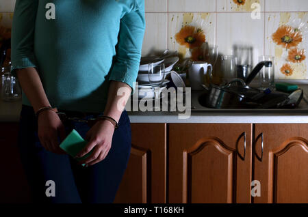 La ragazza ammanettati, orinato e stanco di mano ogni giorno il lavaggio dei piatti, sorge accanto al bancone della cucina e un lavandino che è riempito con un rack dell ONU Foto Stock