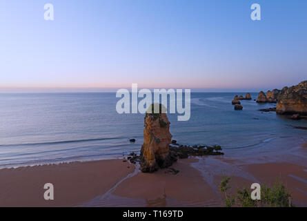 Vuoto spiaggia sabbiosa con un tocco di stravaganza scogliere a sunrise di Lagos, Portogallo. Nuvoloso Tramonto sull'Oceano Atlantico. Foto Stock