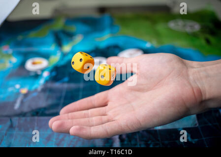 La mano lanci di dadi di colore giallo sul campo di gioco. Buona fortuna e le emozioni. Il concetto dei giochi da tavolo Foto Stock
