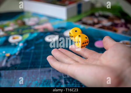 La mano lanci di dadi di colore giallo sul campo di gioco. Buona fortuna e le emozioni. Giochi da tavolo. Momenti di gioco nella dinamica Foto Stock