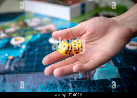 La mano lanci di dadi di colore giallo sul campo di gioco. Buona fortuna e le emozioni. Il concetto dei giochi da tavolo Foto Stock