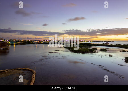 Il sole tramonta sulla Baia di Chetumal off Ambergris Caye Belize casting brillanti tonalità attraverso il cielo, le luci di San Pedro twinkle in distanza. Foto Stock