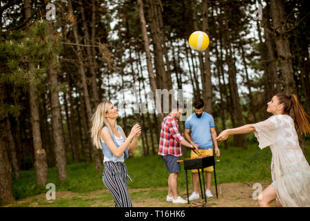 Giovani donne giocando a pallavolo su picnik in primavera la natura mentre gli uomini preparare grill Foto Stock