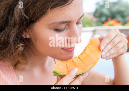 Giovane donna in bianco estate sorridente mangiare orange melone fette di melone al di fuori in Italia villa soleggiata la luce solare Foto Stock