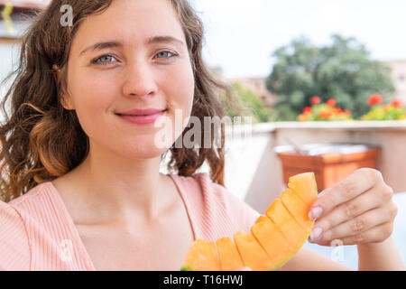 Giovane donna felice in estate bianco mangiare sorridente orange melone fette di melone al di fuori in Italia villa soleggiata la luce solare Foto Stock