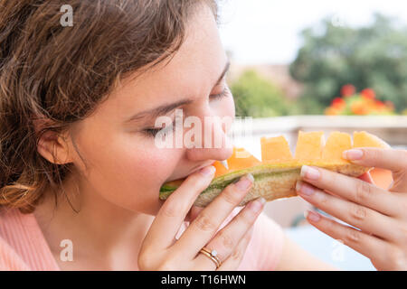 Giovane donna di mordere in estate bianco mangiare orange melone fette di melone al di fuori in Italia villa soleggiata la luce solare Foto Stock