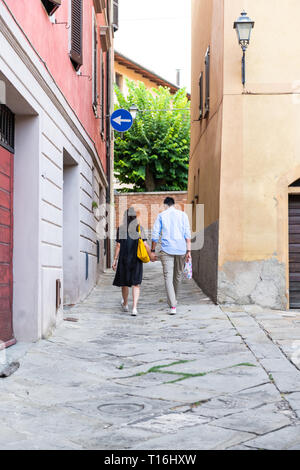 Chiusi, Italia - 25 agosto 2018: Alley Street nel piccolo villaggio di città in Umbria durante il giorno con coppia tenendo le mani a piedi dal giallo arancio un colorato Foto Stock