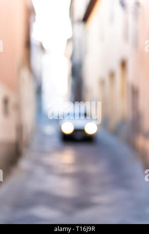 Chiusi, Italia street nel piccolo villaggio di città in Toscana stretta vista verticale con rosa arancione pareti gialle e guida auto fari abstract bokeh di fondo blu Foto Stock