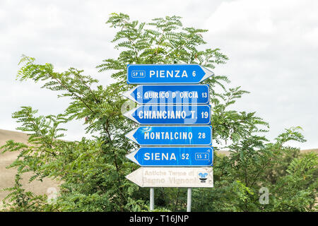 Monticchiello, Italia - 26 agosto 2018: Villaggio Città in Toscana durante il giorno d'estate e di sole e autostrada strada con blue uscita direzione segno per Pien Foto Stock