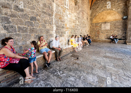 San Gimignano, Italia - 27 agosto 2018: Molte persone sedute in appoggio sulle panchine in piccola e antica città medievale Borgo in Toscana durante il giorno di estate Foto Stock