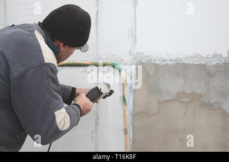 Un anziano operaio trapani un foro in una parete in polistirolo espanso per l'installazione successiva di un rinforzo di plastica il grano. Creazione di fori nel muro con un Foto Stock