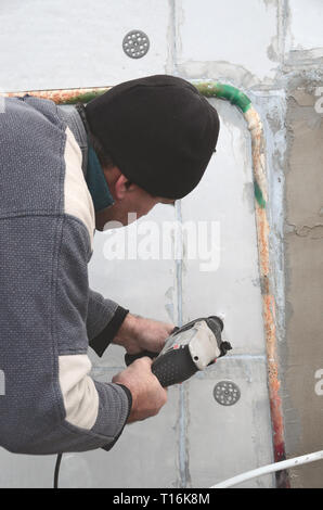 Un anziano operaio trapani un foro in una parete in polistirolo espanso per l'installazione successiva di un rinforzo di plastica il grano. Creazione di fori nel muro con un Foto Stock