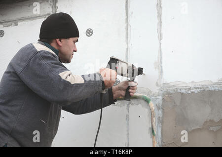 Un anziano operaio trapani un foro in una parete in polistirolo espanso per l'installazione successiva di un rinforzo di plastica il grano. Creazione di fori nel muro con un Foto Stock