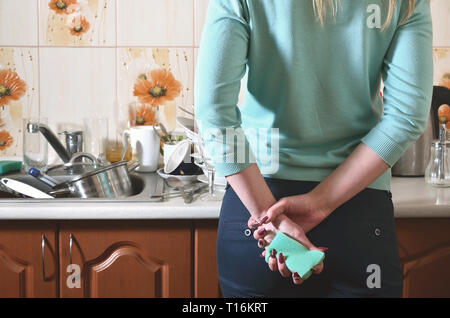 Frammento del corpo femminile presso il bancone cucina, riempito con un sacco di piatti non lavati. La ragazza è stanco di affrontare il compito quotidiano di lavaggio d Foto Stock