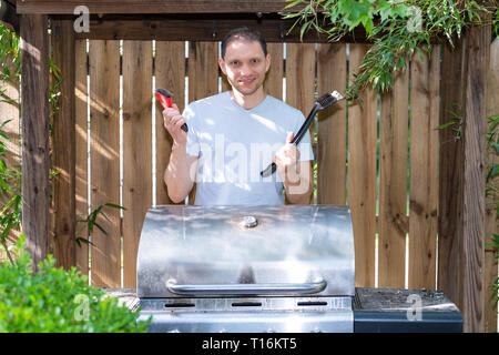 Grigliata bbq nuovo moderno grill in natura all'aperto d'estate il parco o giardino nel cortile sulla giornata soleggiata con uomo in piedi di attrezzatura di tenuta Foto Stock