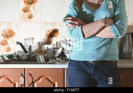 Frammento del corpo femminile presso il bancone cucina, riempito con un sacco di piatti non lavati. La ragazza è stanco di affrontare il compito quotidiano di lavaggio d Foto Stock