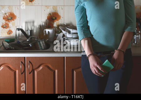 La ragazza ammanettati, orinato e stanco di mano ogni giorno il lavaggio dei piatti, sorge accanto al bancone della cucina e un lavandino che è riempito con un rack dell ONU Foto Stock