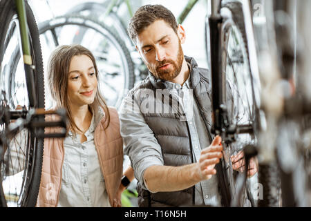 Venditore aiutare giovani donne a scegliere una nuova bicicletta per acquistare in piedi nel negozio di biciclette Foto Stock