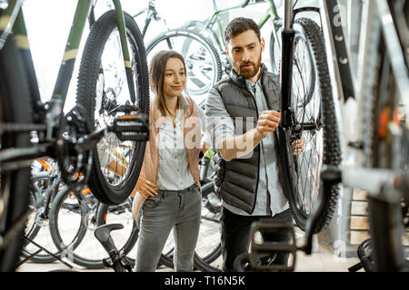 Venditore aiutare giovani donne a scegliere una nuova bicicletta per acquistare in piedi nel negozio di biciclette Foto Stock