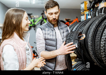 Venditore aiutare giovani donne a scegliere un nuovo pneumatico di una bicicletta nel negozio di articoli sportivi Foto Stock