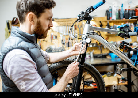 Repairman serve una bicicletta, il controllo di una pressione di aria nell'ammortizzatore pneumatico di una forcella in officina Foto Stock