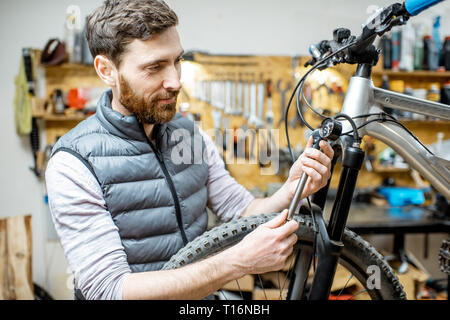 Repairman serve una bicicletta, il controllo di una pressione di aria nell'ammortizzatore pneumatico di una forcella in officina Foto Stock