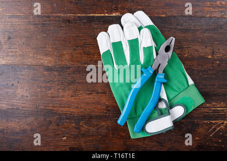 Guanti da lavoro e strumenti di falegname giacciono su un marrone tavolo in legno. vista da sopra. spazio per il testo Foto Stock