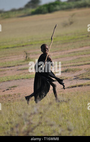 IGUNGA, Tanzania - 6 febbraio 2012:un bambino della tribù Wataturu corre intorno in un campo con un bastone nella sua mano. Foto Stock