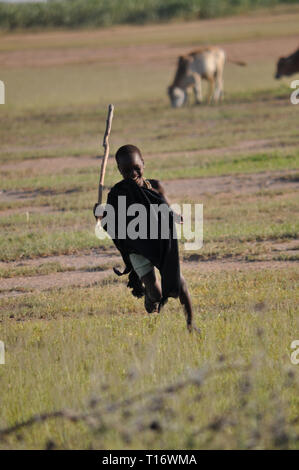 IGUNGA, Tanzania - 6 febbraio 2012:un bambino della tribù Wataturu corre intorno in un campo con un bastone nella sua mano. Foto Stock