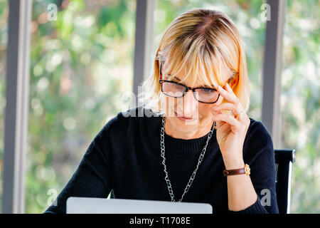 40s senior imprenditrice caucasica concentrare e fissando il computer portatile in ambiente office Foto Stock